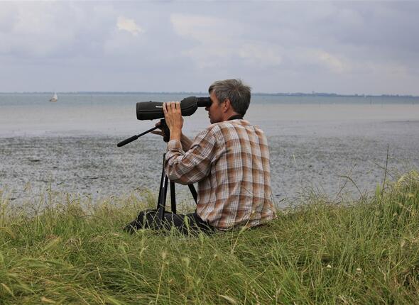 Vogelaar zittend in gras met spot scope bestudeert het gedrag van vogels aan de vloedlijn